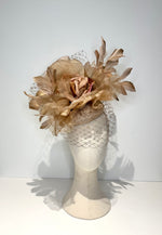 Decorative headpiece with gold flowers and feathers on a mannequin head against a white background