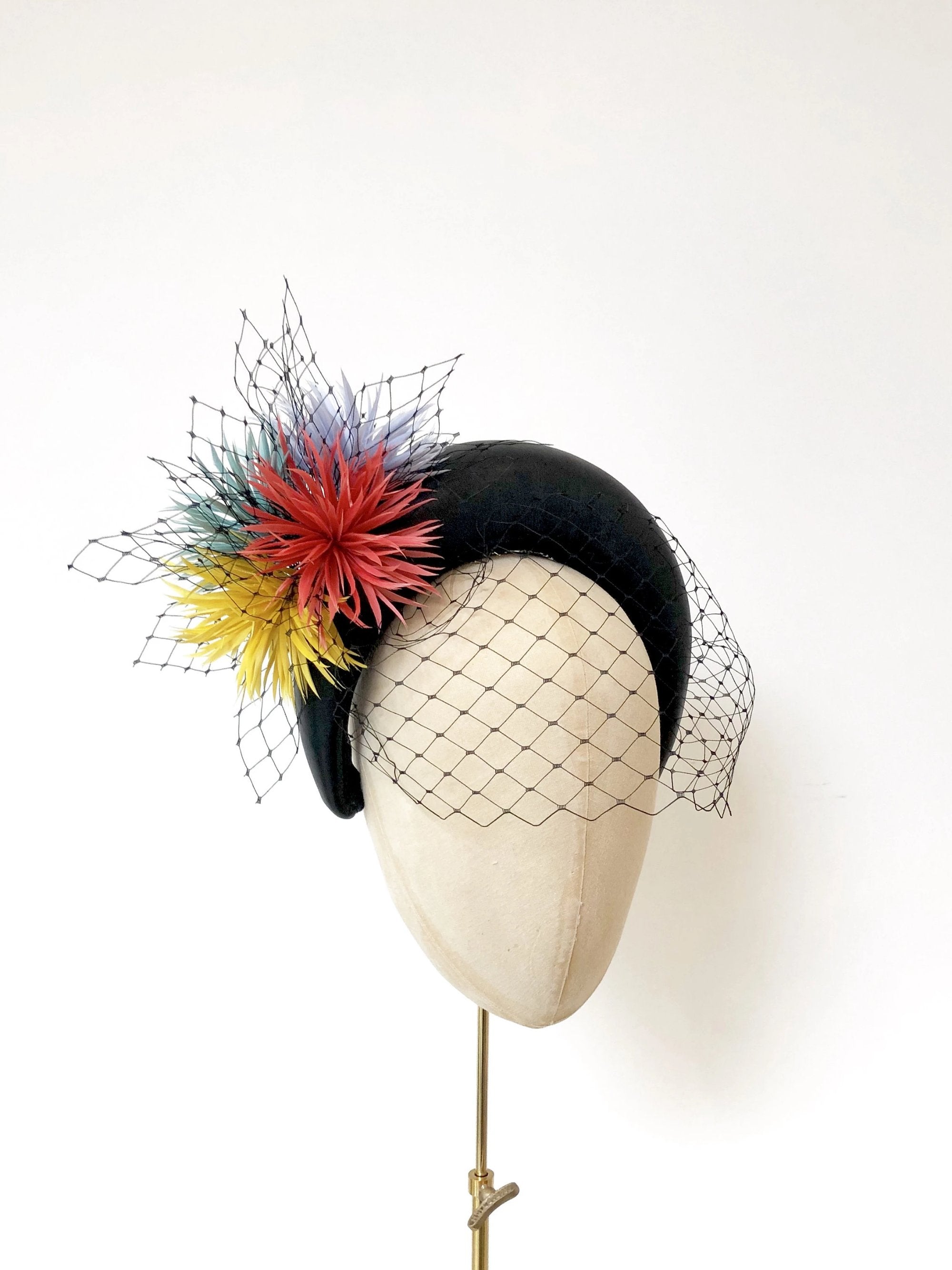 black leather padded halo crown headband, with coral, yellow, green and blue spikey feather flowers and black widow veiling
