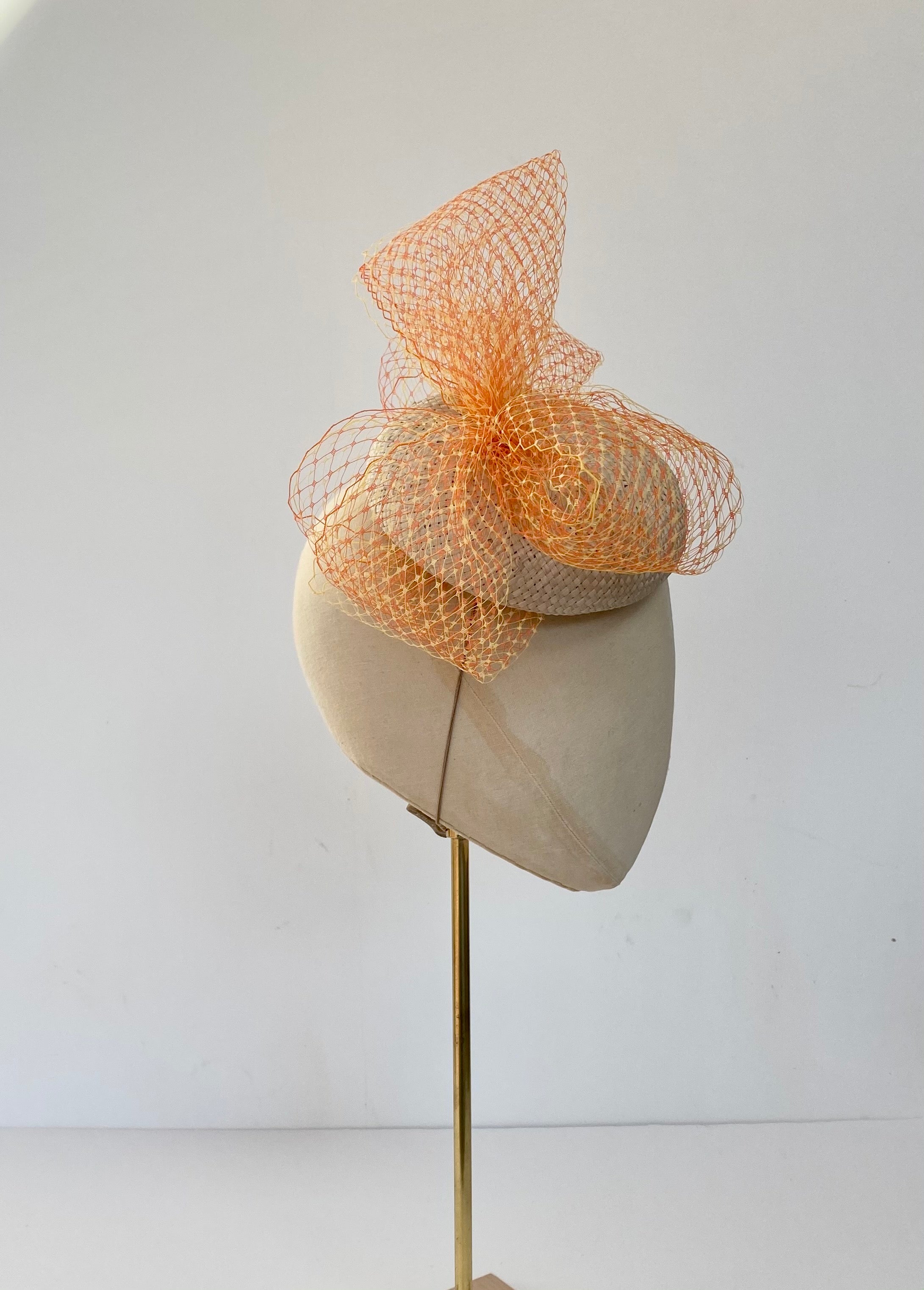 natural ivory button cocktail hat for wedding guest mother of the bride, with bright coloured veiling bow in orange and yellow